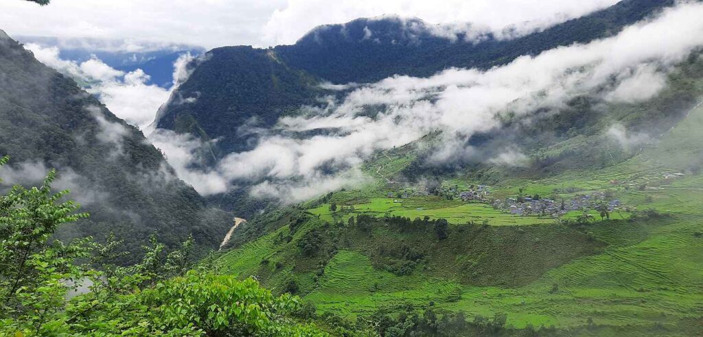 Lush green hills and a village covered in clouds along the Upper Arun Valley Trek route in eastern Nepal.”
