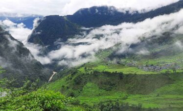 Lush green hills and a village covered in clouds along the Upper Arun Valley Trek route in eastern Nepal.”