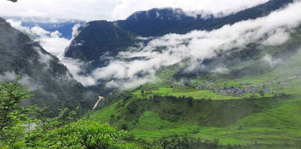 Lush green hills and a village covered in clouds along the Upper Arun Valley Trek route in eastern Nepal.”