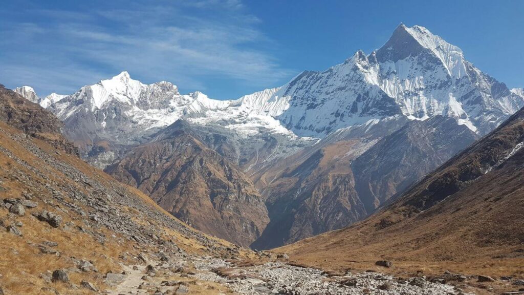 Machhapuchhre (Fishtail) and snowy Himalayan peaks under a blue sky above the rocky trail to Annapurna Base Camp, Nepal