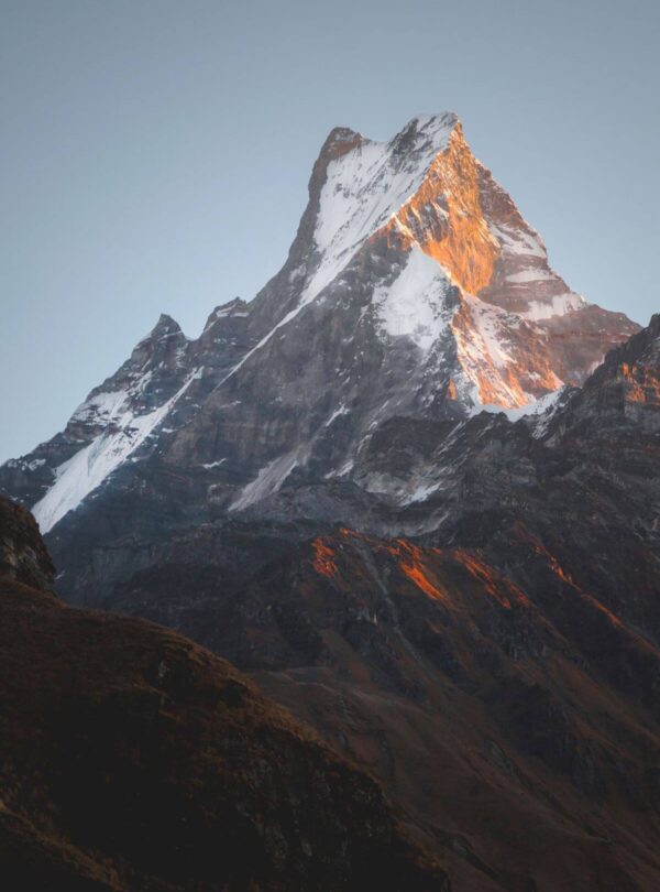 First sunlight turning the summit of Machhapuchhre (Fishtail) orange above dark ridges on the Mardi Himal Trek, Nepal
